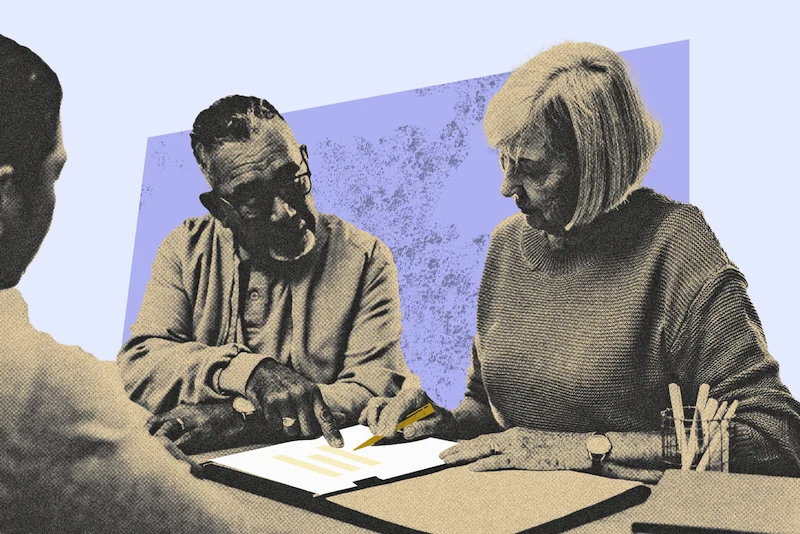 An older couple reviews estate planning documents with a professional, highlighting information on a clipboard.
