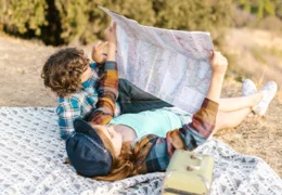 two kids lying down on picnic blanket while looking at a map